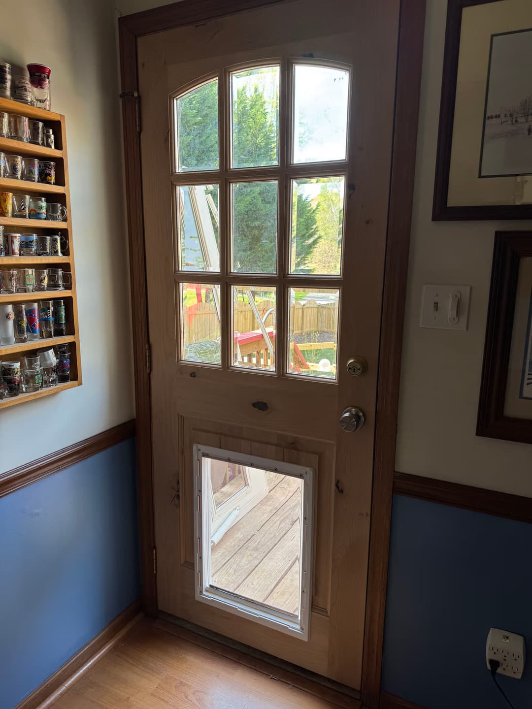 Wooden door with windows and a pet door leading to a deck, framed by colorful spices on the wall.