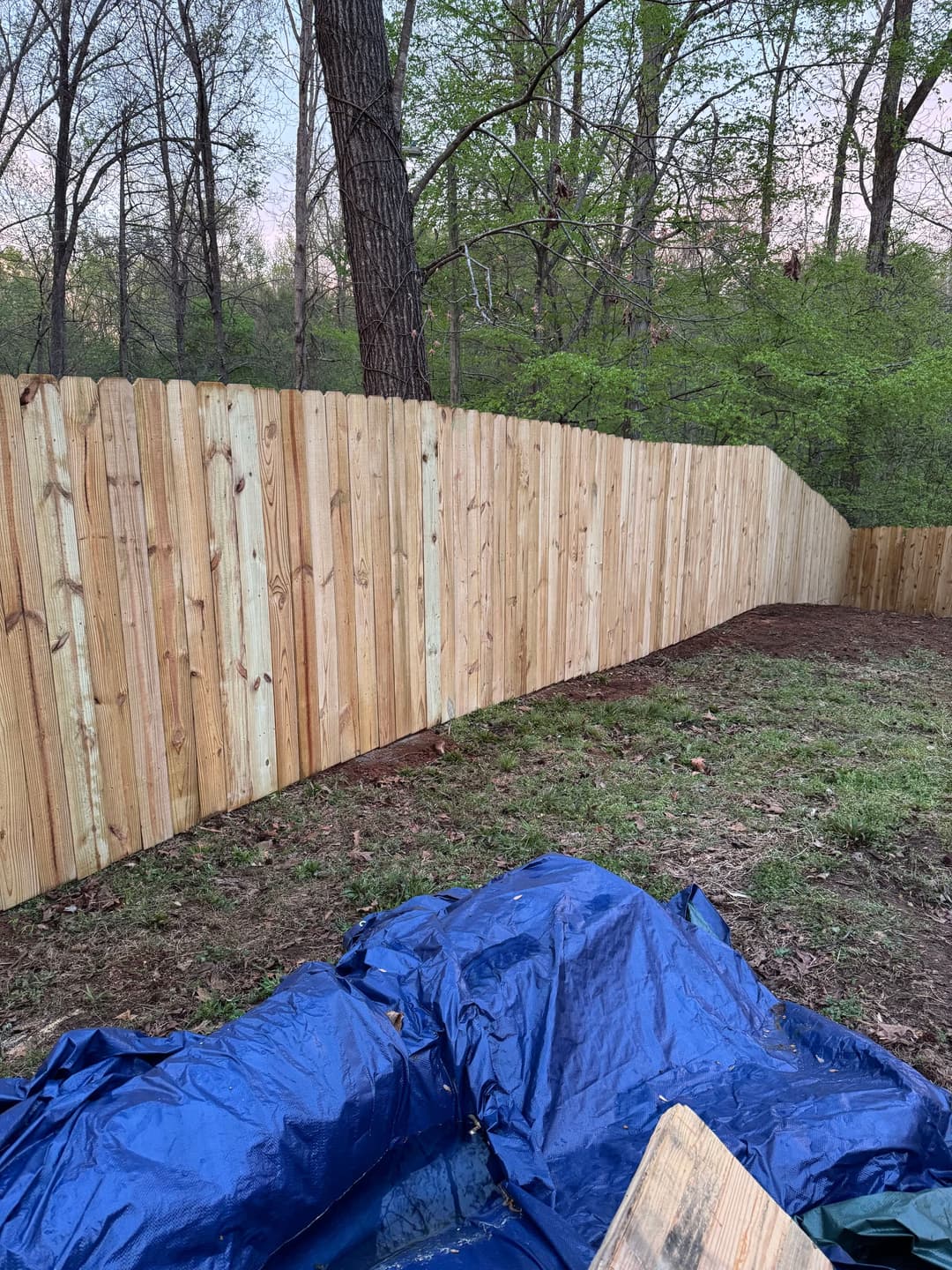 Wooden fence installed in a forested area with blue tarp on the ground.