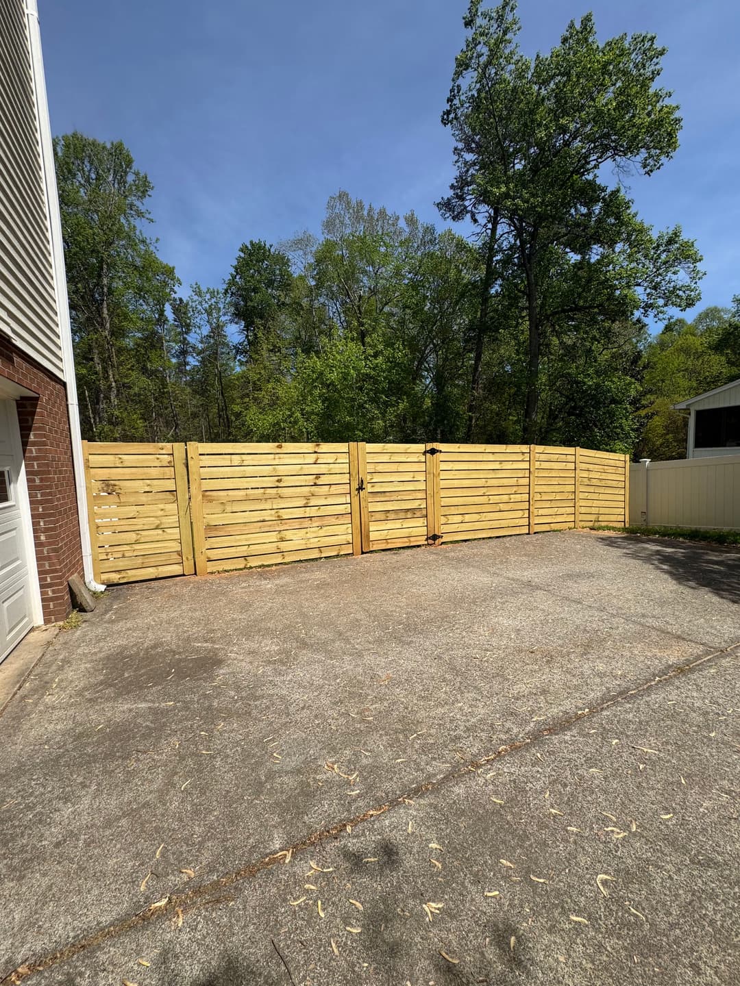 New wooden privacy fence in a backyard with concrete driveway and trees in the background.