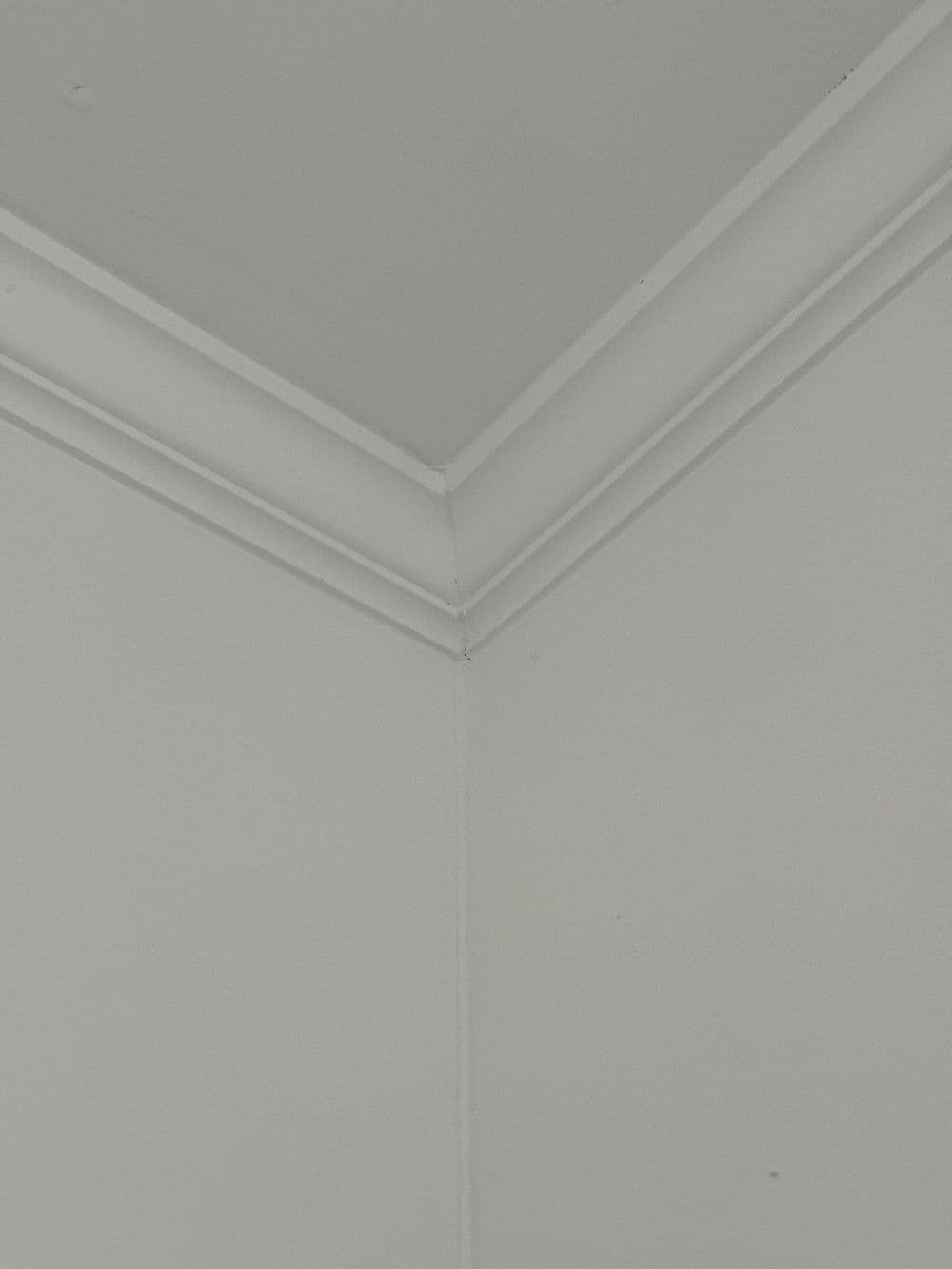 White ceiling corner with detailed molding and smooth surfaces. Clean and minimalist design.