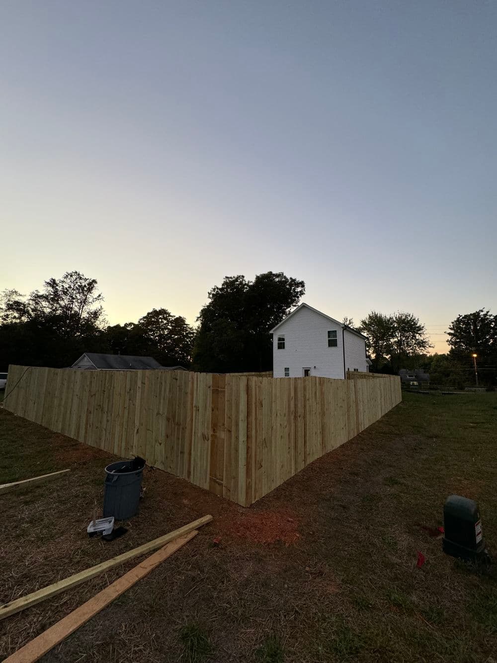 New wooden fence in a yard with a house and trees at dusk, showcasing home improvement.