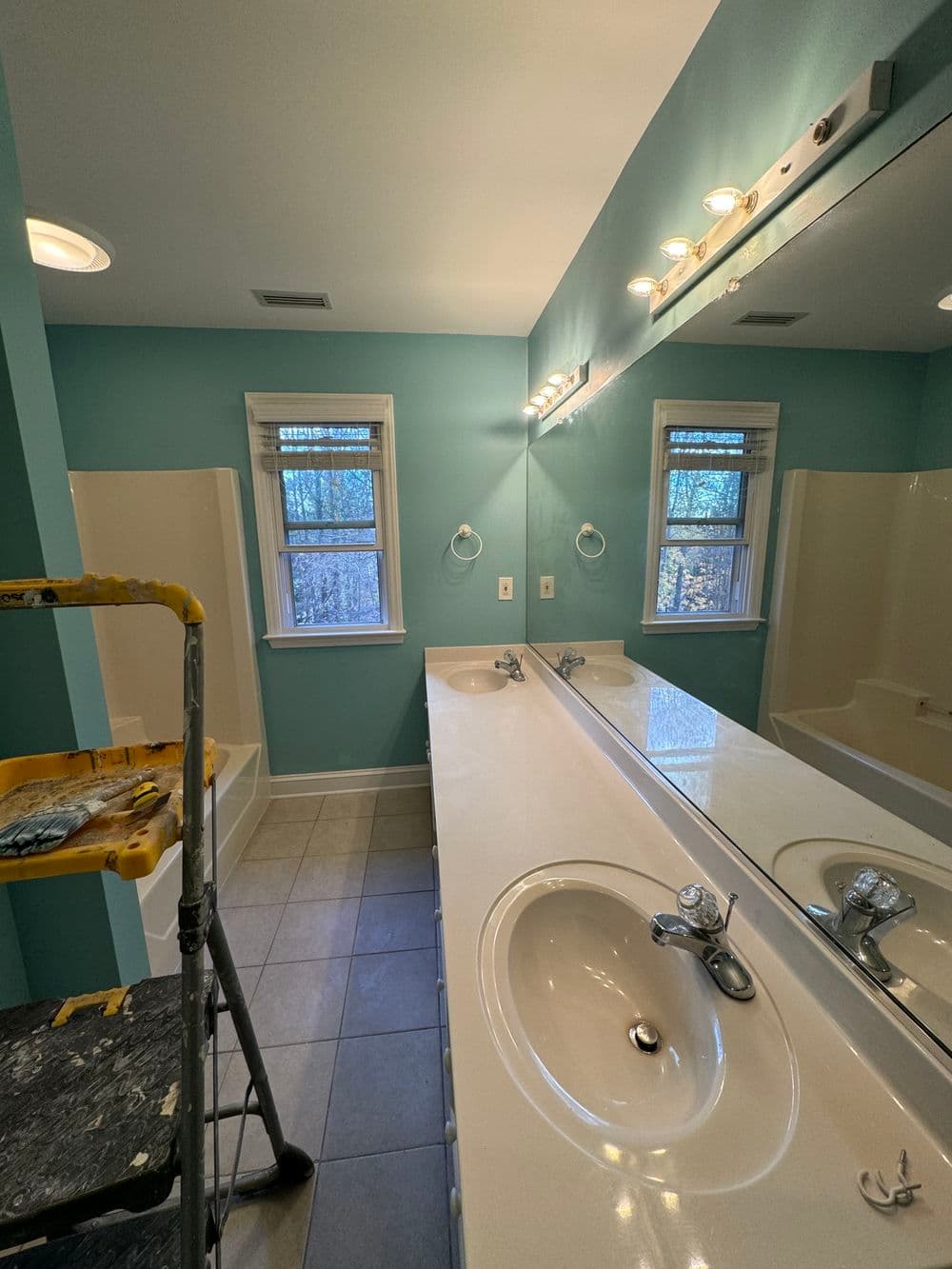 Renovated bathroom with blue walls, dual sinks, and natural light from window.