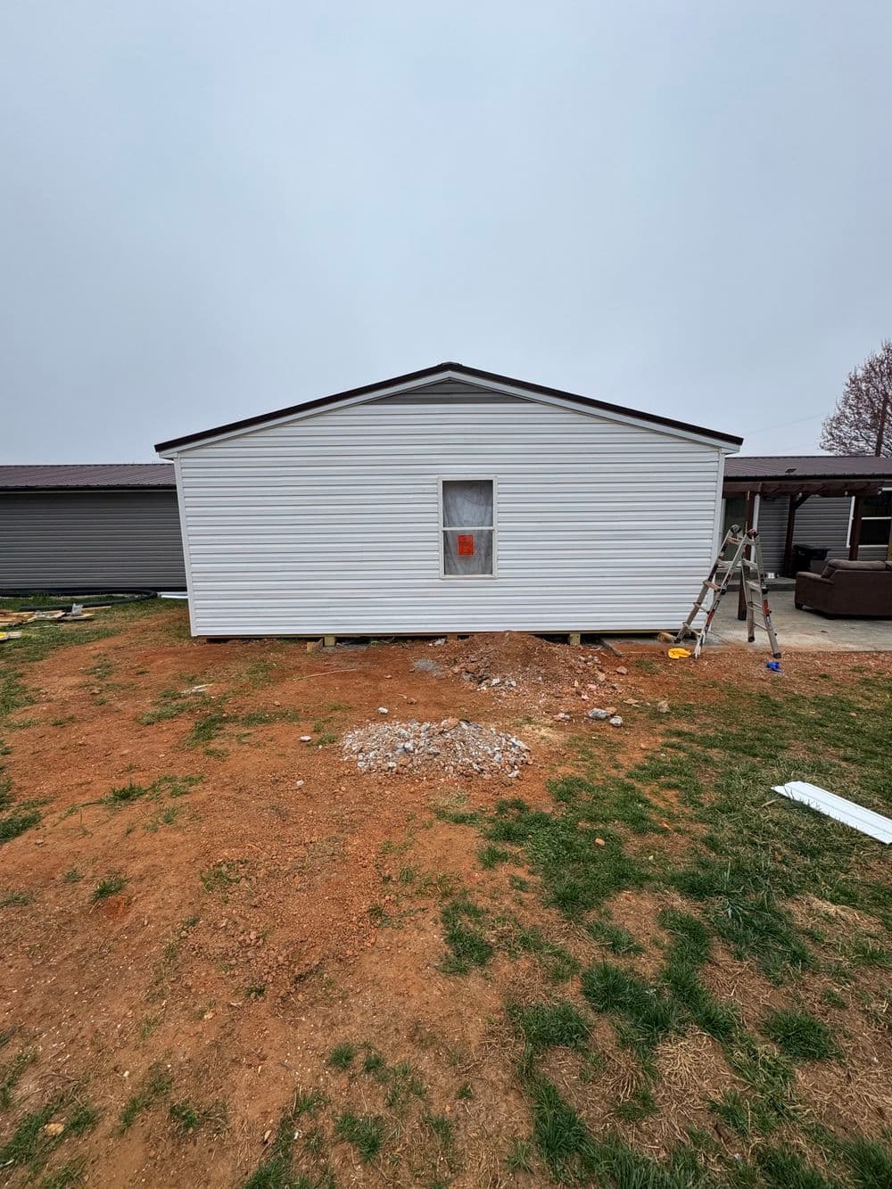 Exterior of a newly renovated white mobile home with a single window and construction tools nearby.