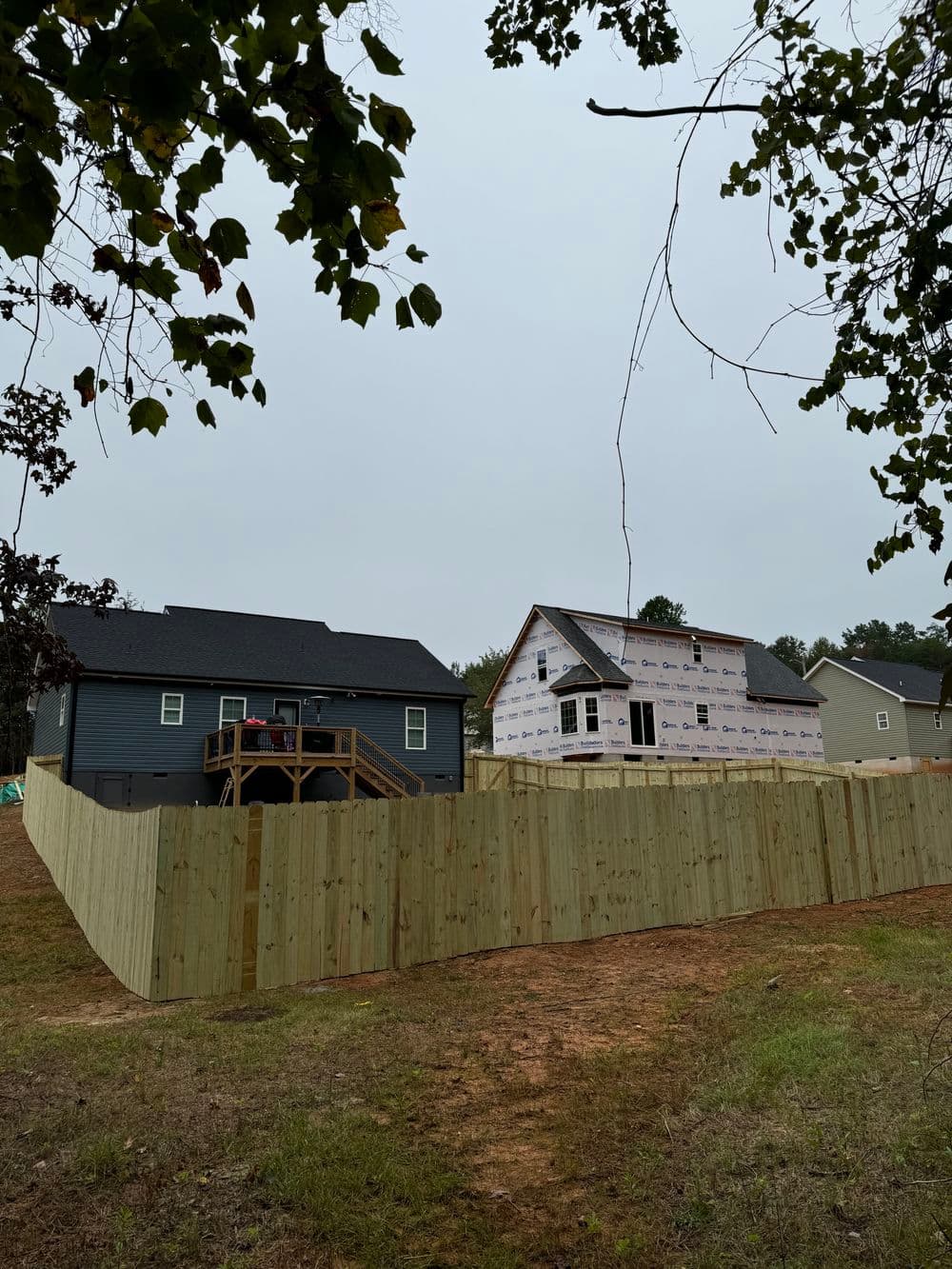 New houses under construction with wooden fences in a residential neighborhood.