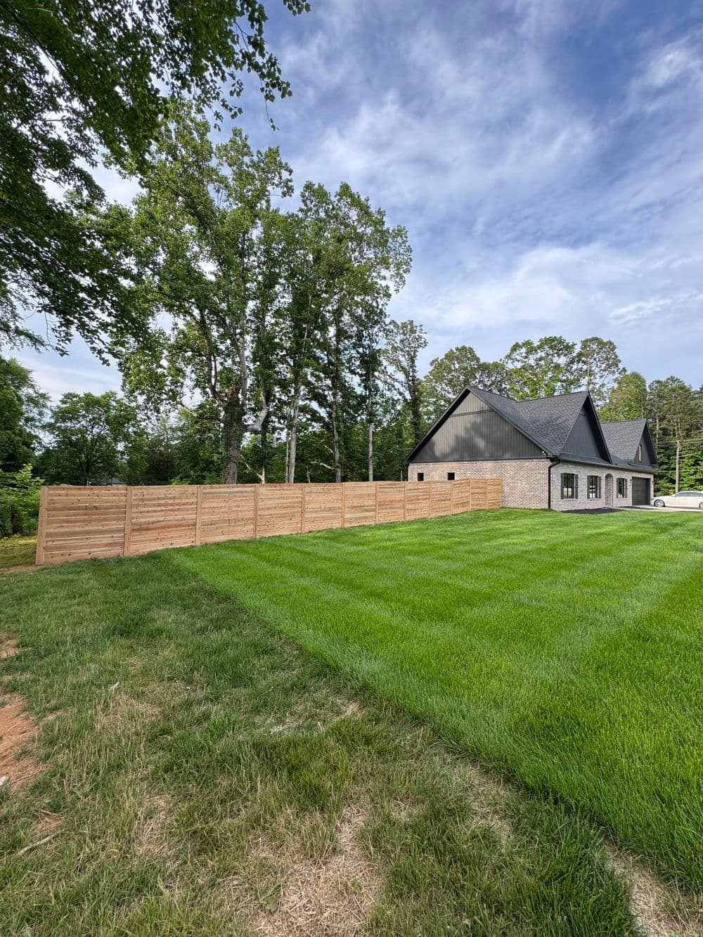 Modern house with a black roof surrounded by a wooden fence and lush green lawn.