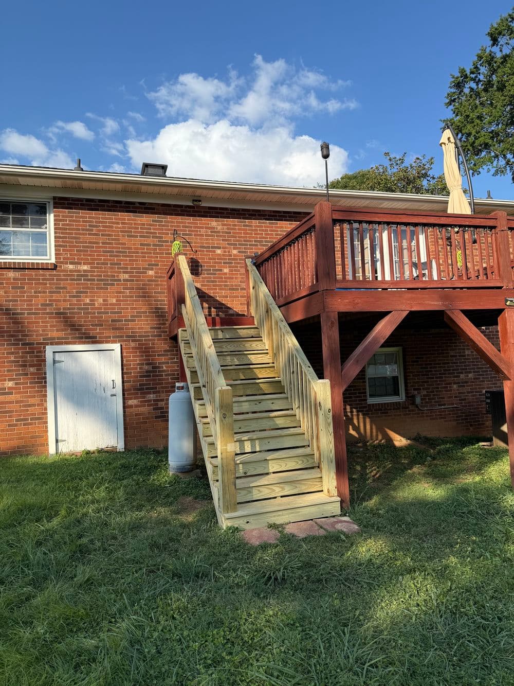 Wooden stairs leading to a red wooden deck on a brick house with green grass and blue sky.