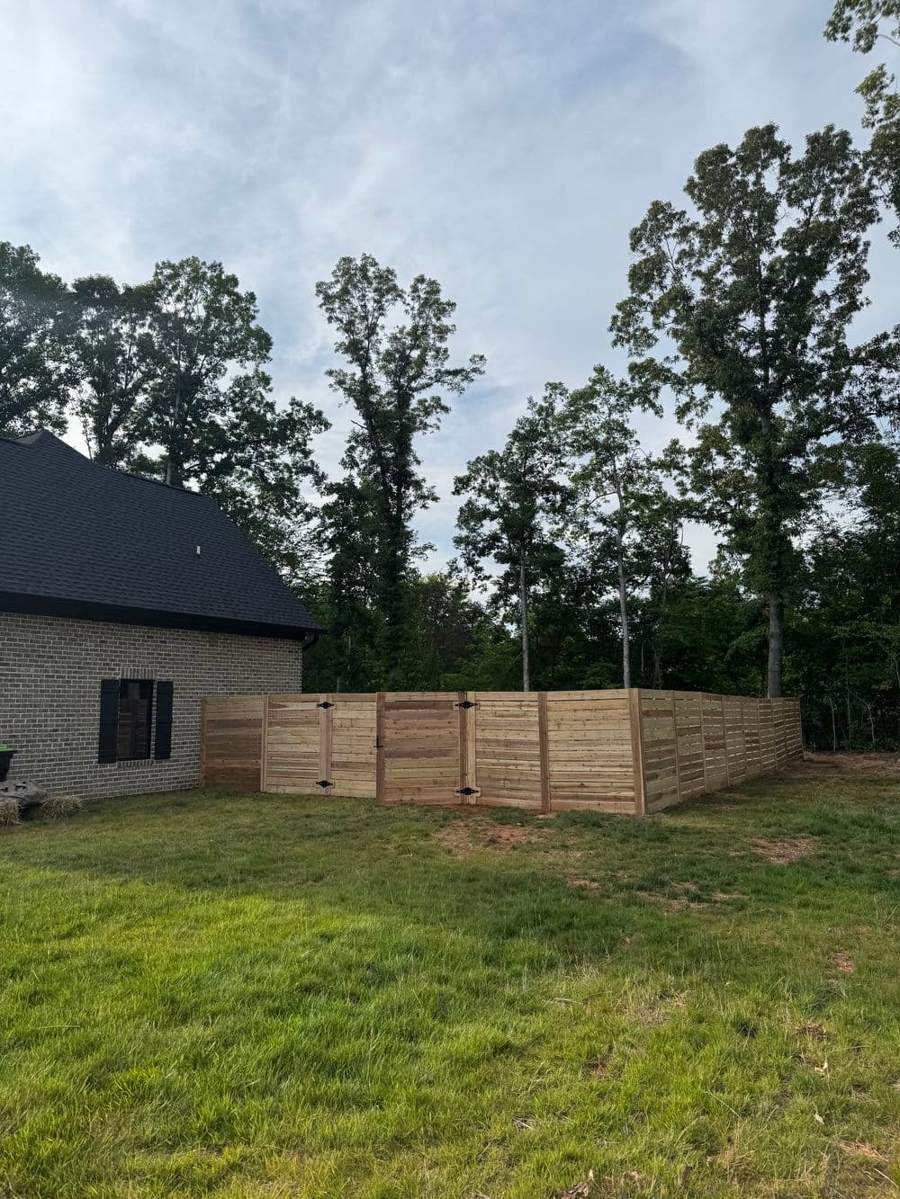 Wooden privacy fence enclosing backyard, surrounded by green grass and trees, sunny outdoor setting.