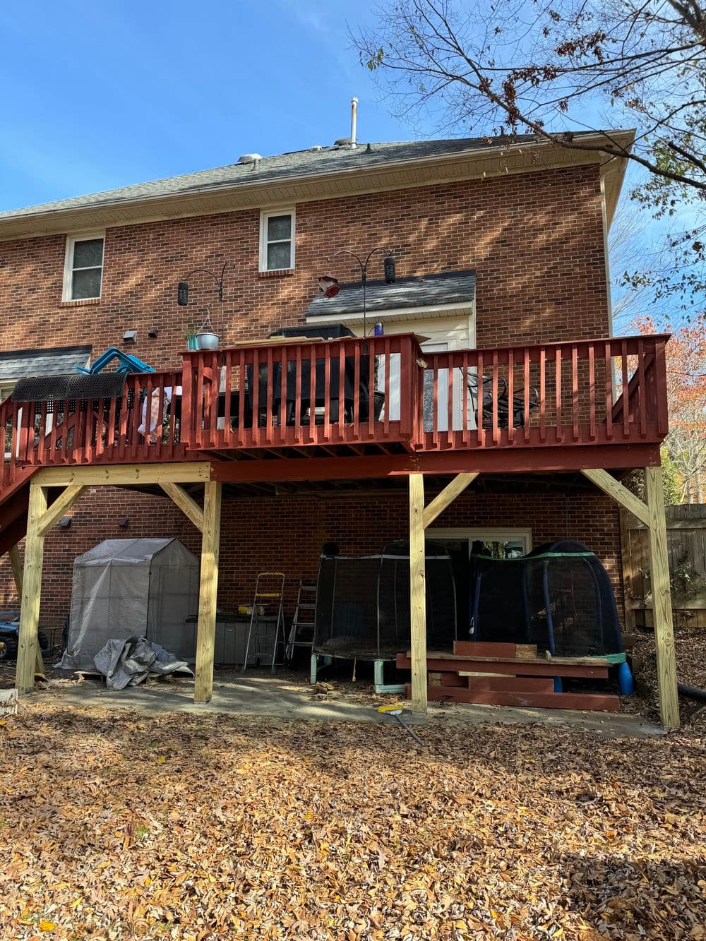Red wooden deck above a patio with storage and outdoor furniture in a residential backyard.