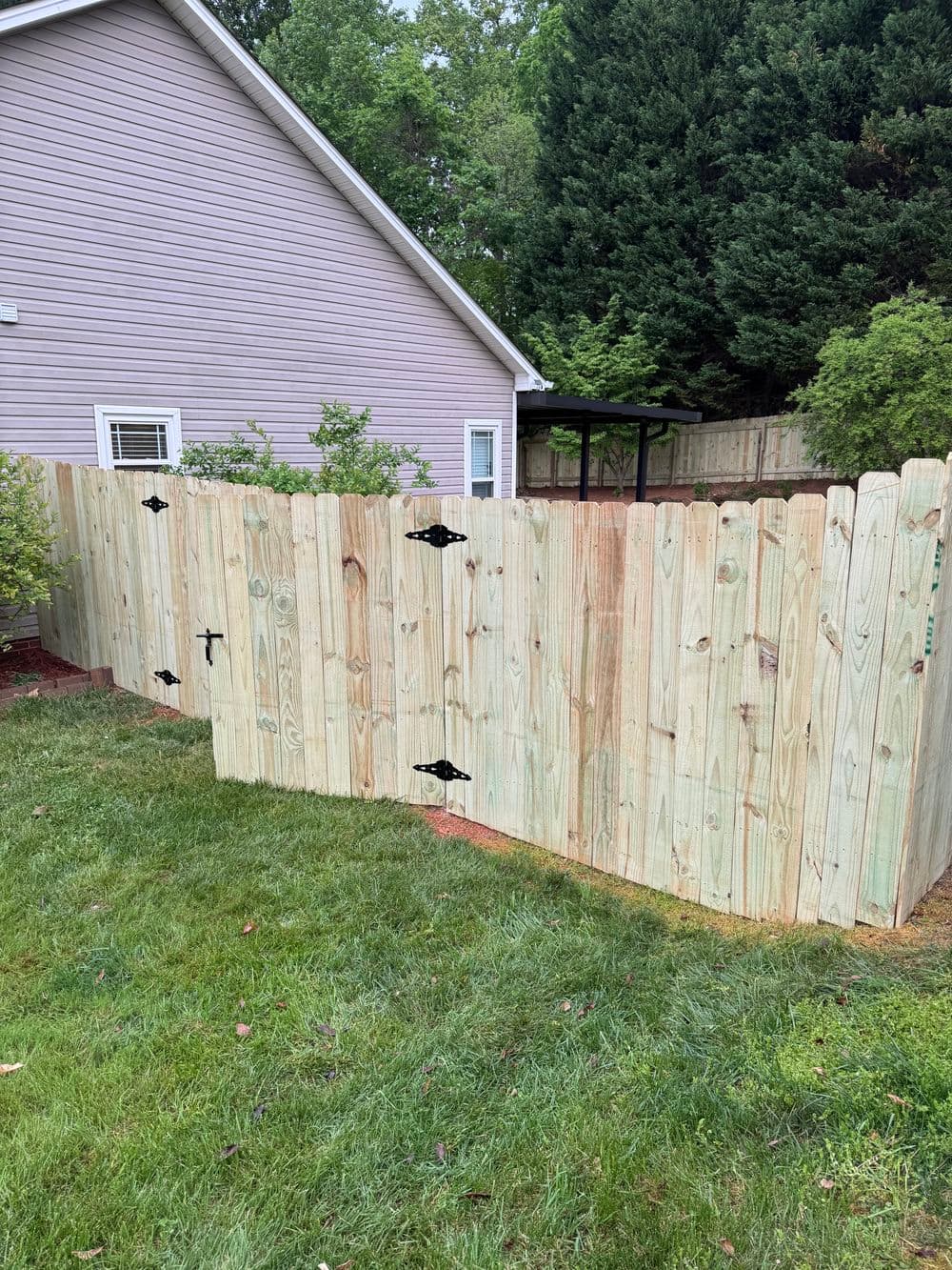 Wooden privacy fence enclosing a backyard with lush green grass and a house in the background.