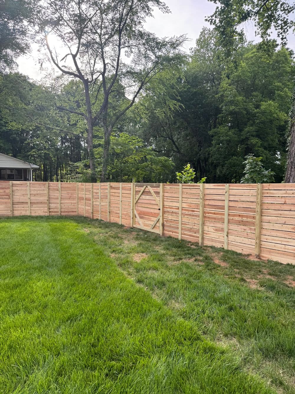 Wooden fence in a backyard with green grass and trees in the background.