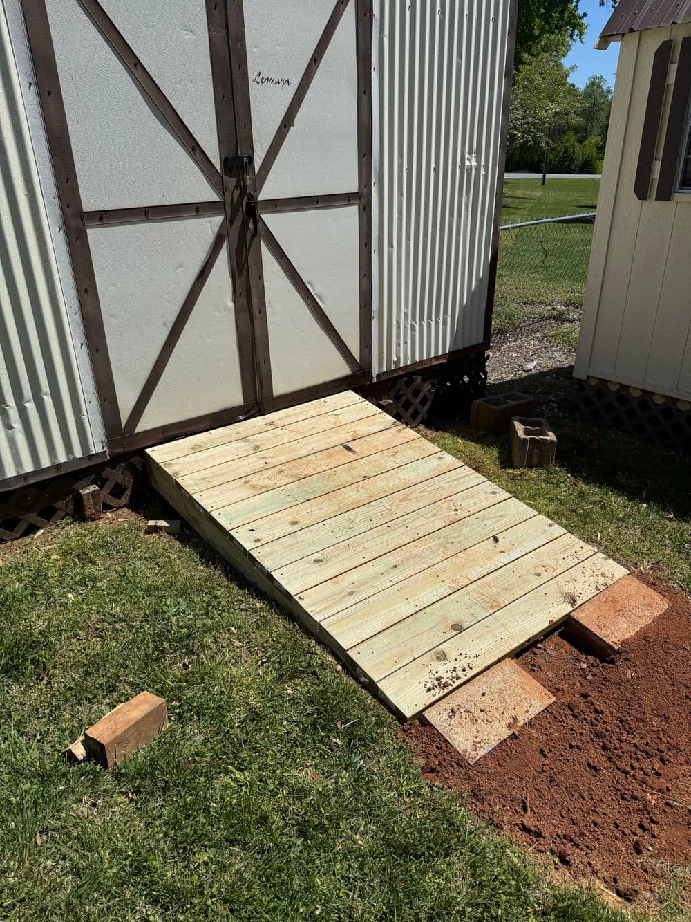 Wooden ramp leading to a shed, set on grass with bricks, promoting accessibility and storage.