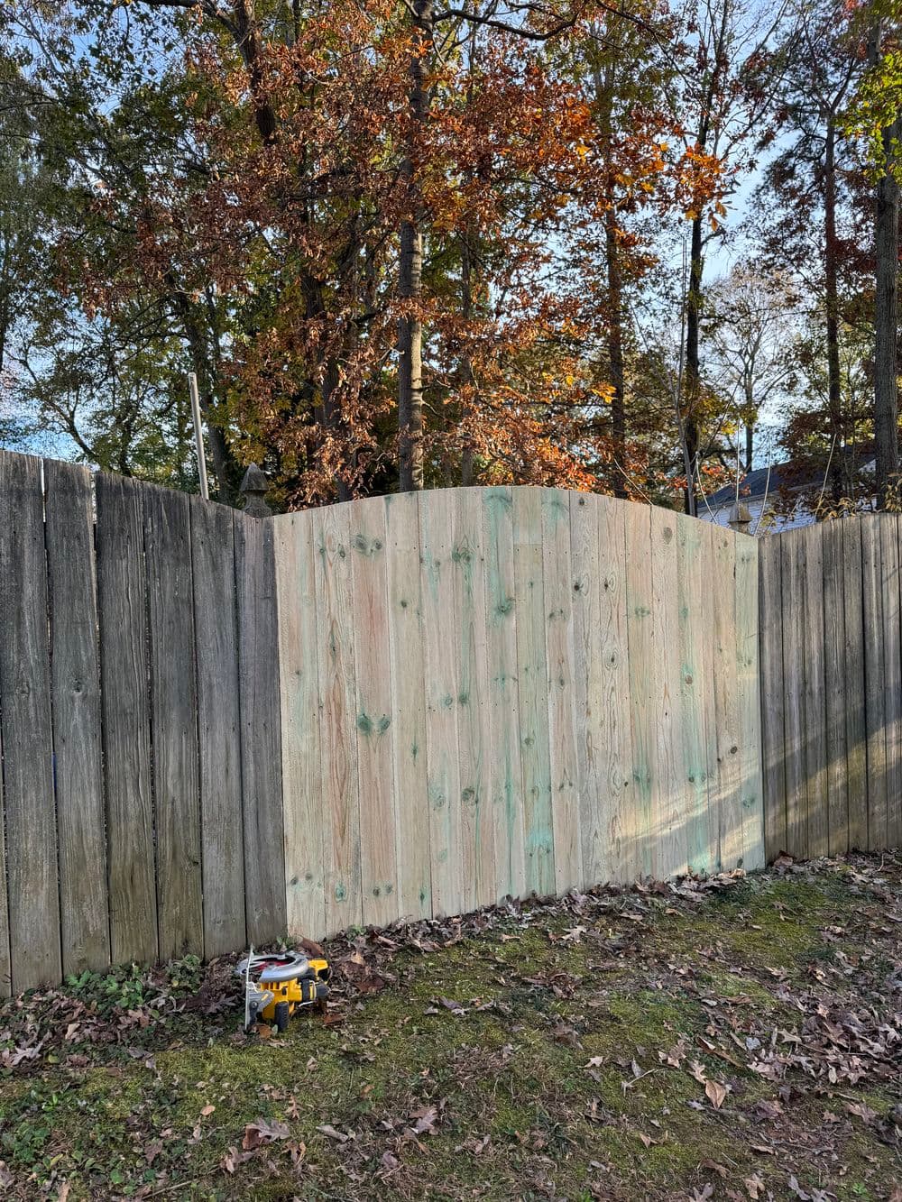 Newly constructed wooden fence section with curved top in autumn setting.