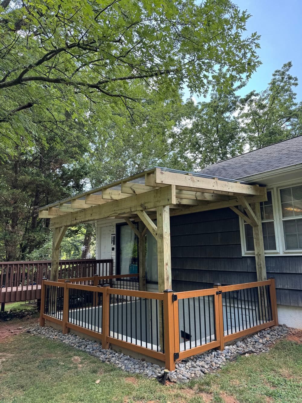 Wooden porch structure with railing, surrounded by trees, beside a house. Ideal outdoor space.