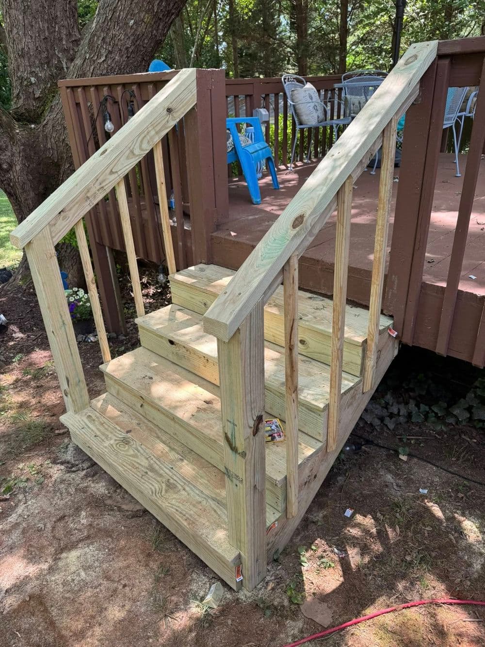 Wooden stairs with handrails leading to a deck in a forested backyard setting.