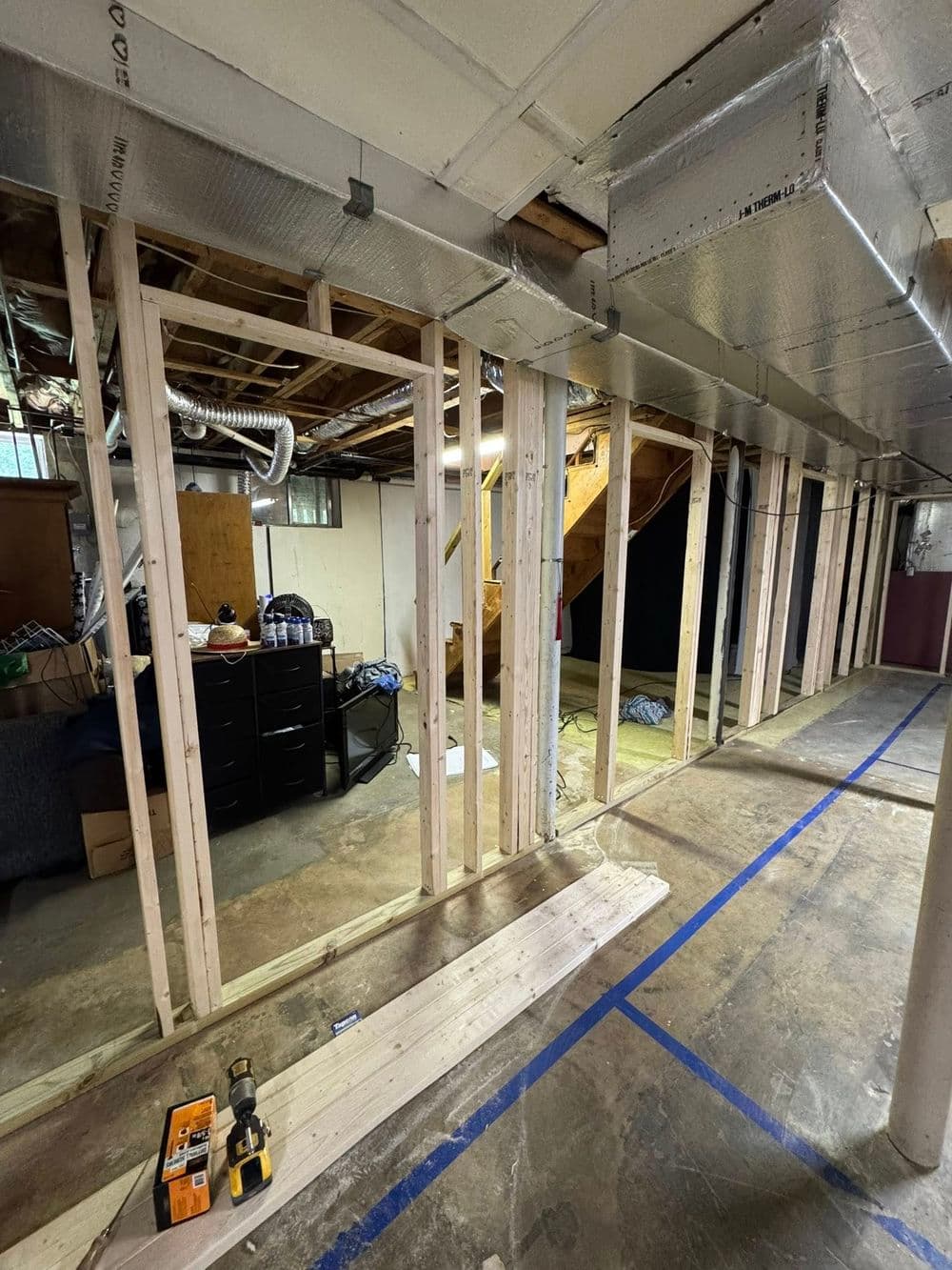 Basement renovation in progress with framed walls, unfinished flooring, and stacked materials.