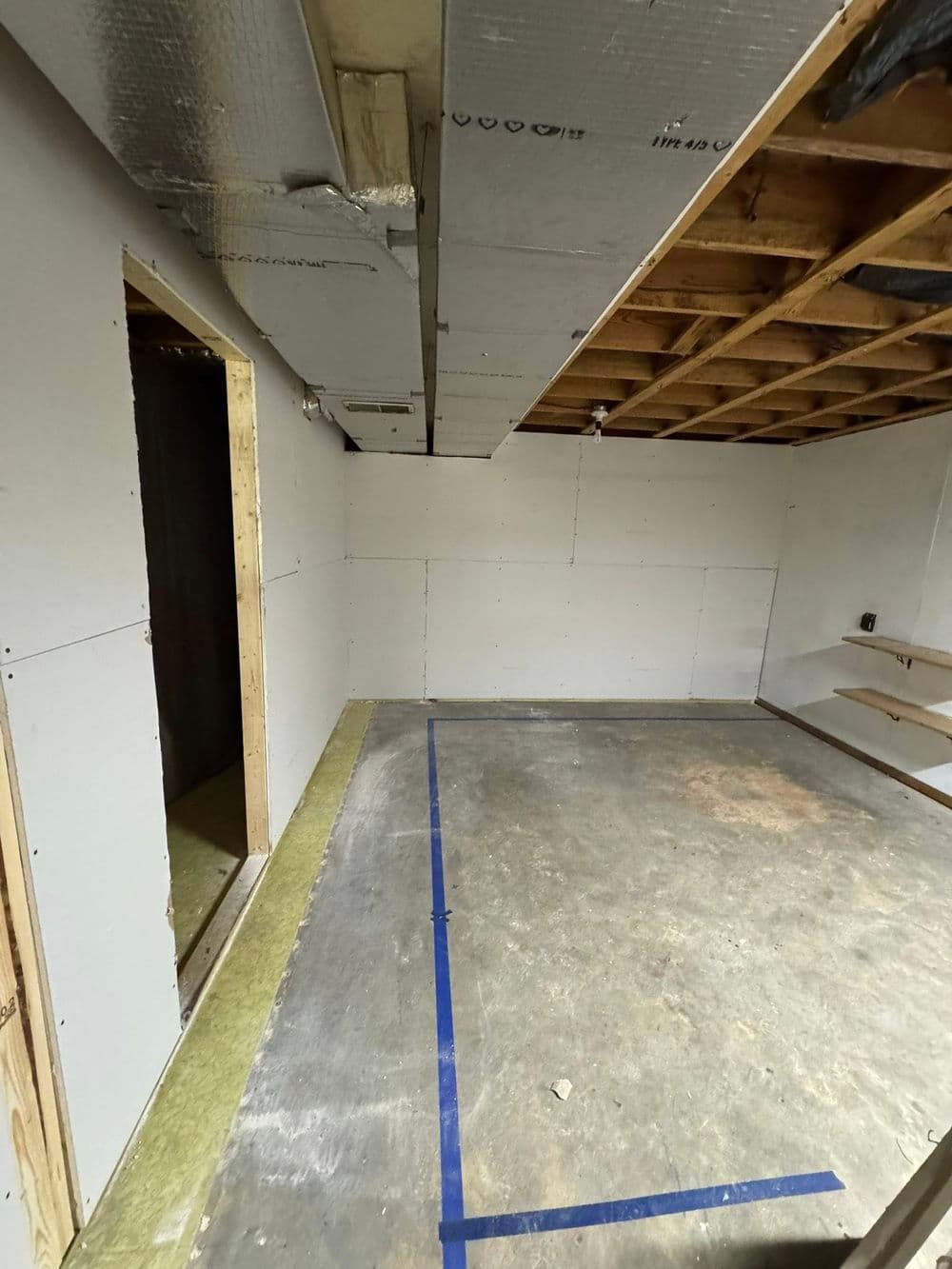 Home renovation progress in a partially drywalled basement with exposed beams and concrete floor.