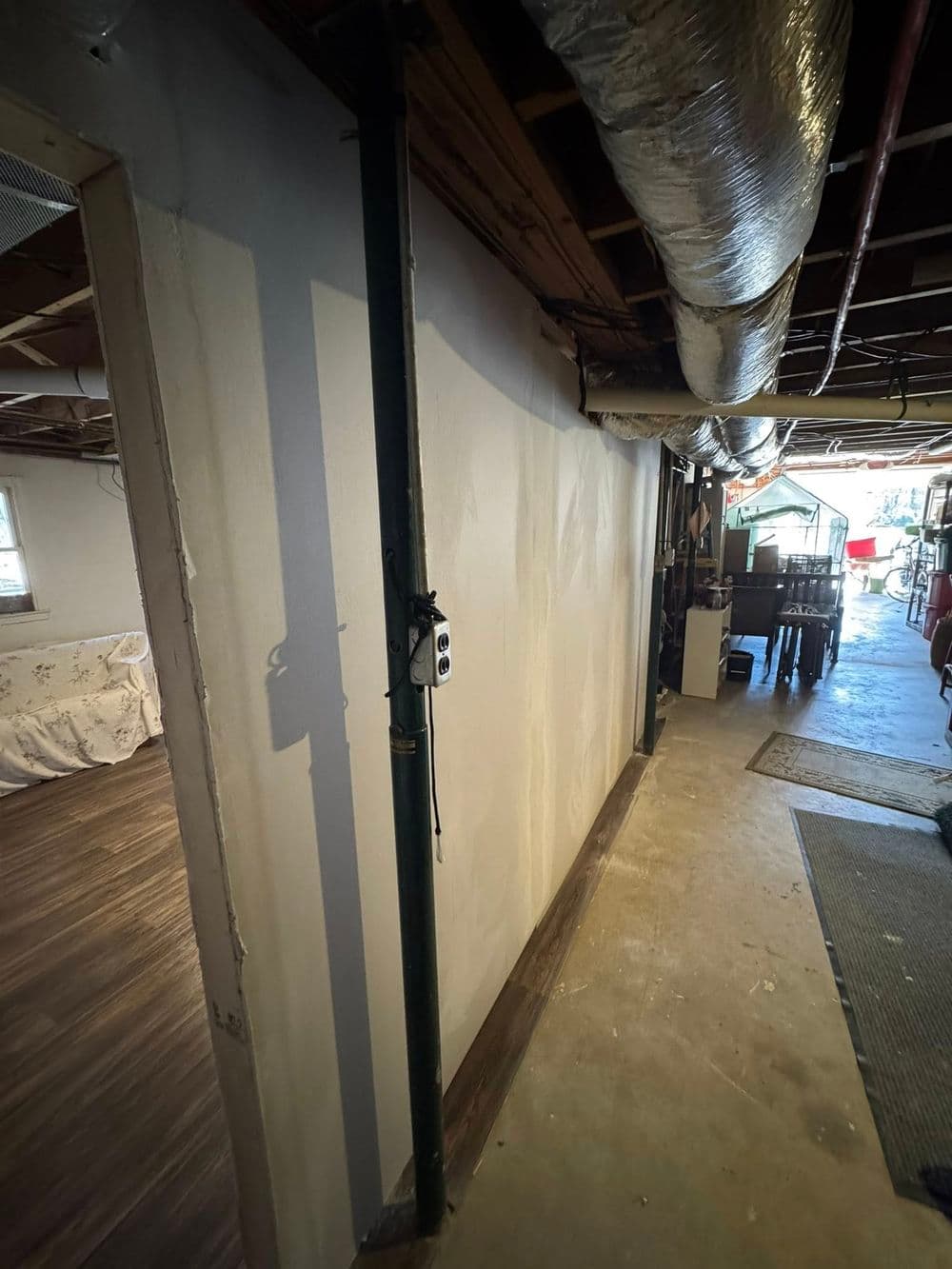 Basement hallway with wall, green pipe, and exposed ceiling ductwork in a residential setting.