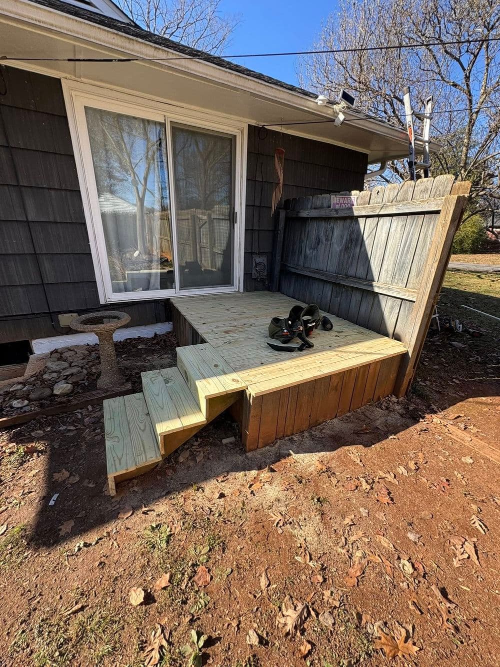 New wooden deck with steps and a sliding glass door, surrounded by a yard and fence.